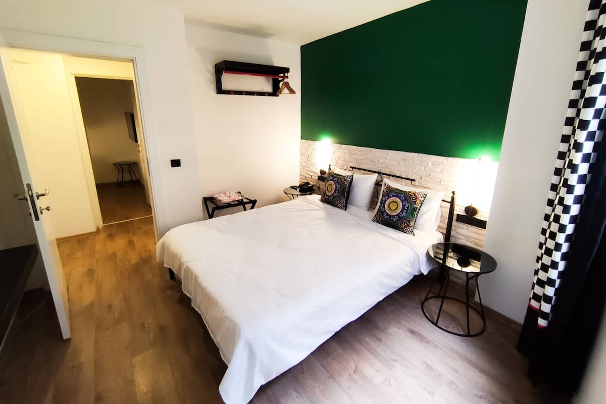 A hotel room with a large bed, a bedside table with a lamp, a small table with a phone, and a green accent wall.