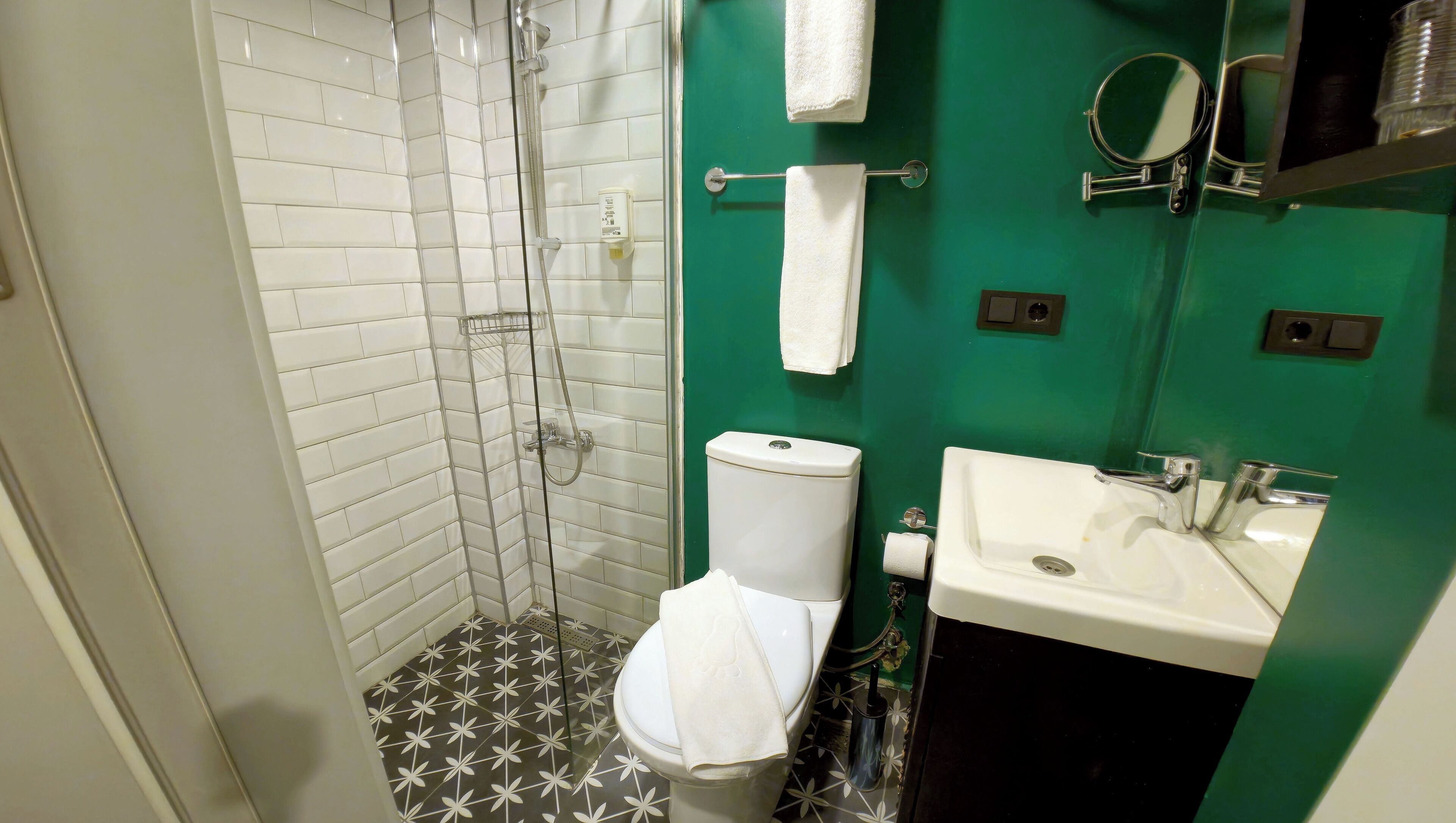 A bathroom with a shower, toilet, sink, and green walls.