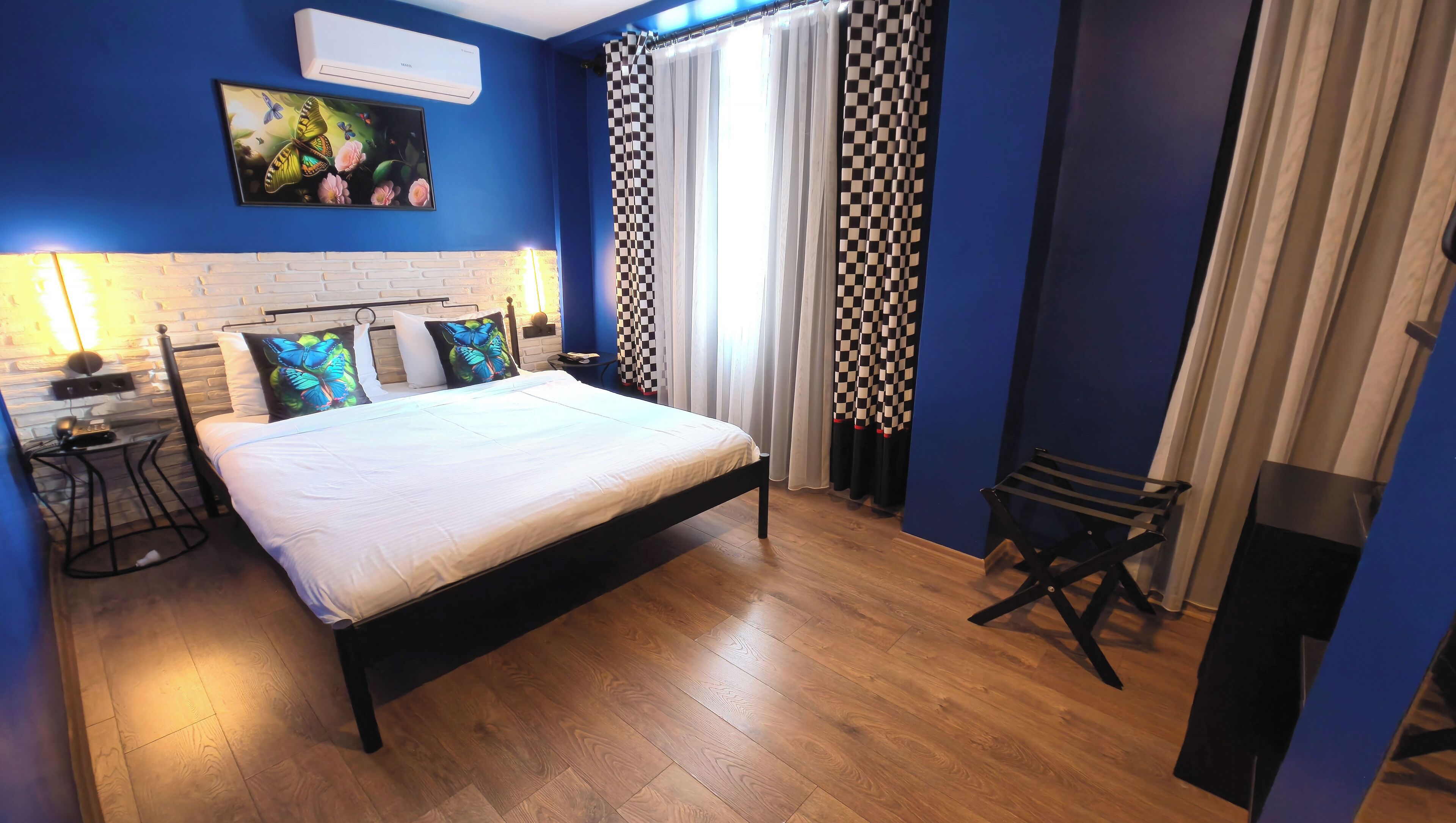 A bedroom with a bed, a nightstand, a lamp, a checkered curtain, and a wooden floor.