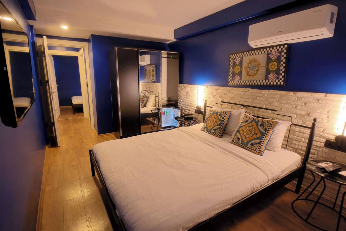 A hotel room with a bed, a desk, a chair, a wardrobe, and a mirror.