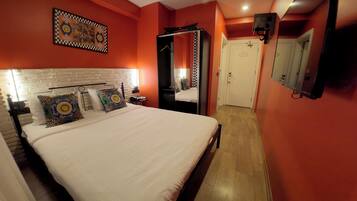 A hotel room with a large bed, a white headboard, a mirror, and a checkered wall hanging.
