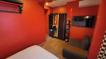 Una habitación de hotel con cama, zona de estar, armario, televisor y espejo.
