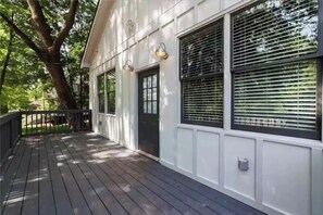 Une terrasse en bois avec un bâtiment blanc doté de grandes fenêtres et d’une porte noire.