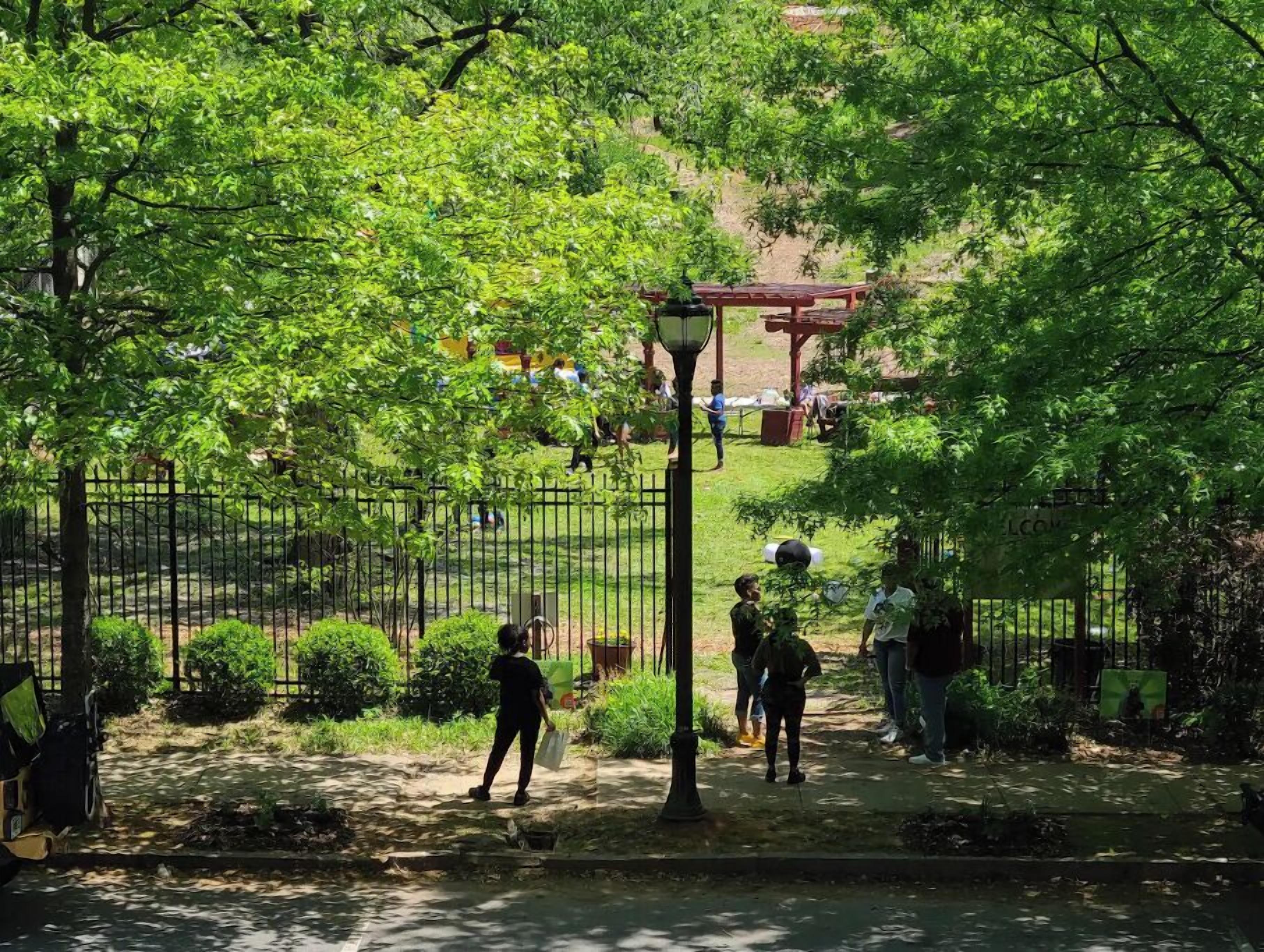A park with a metal fence, trees, and a red structure in the background.