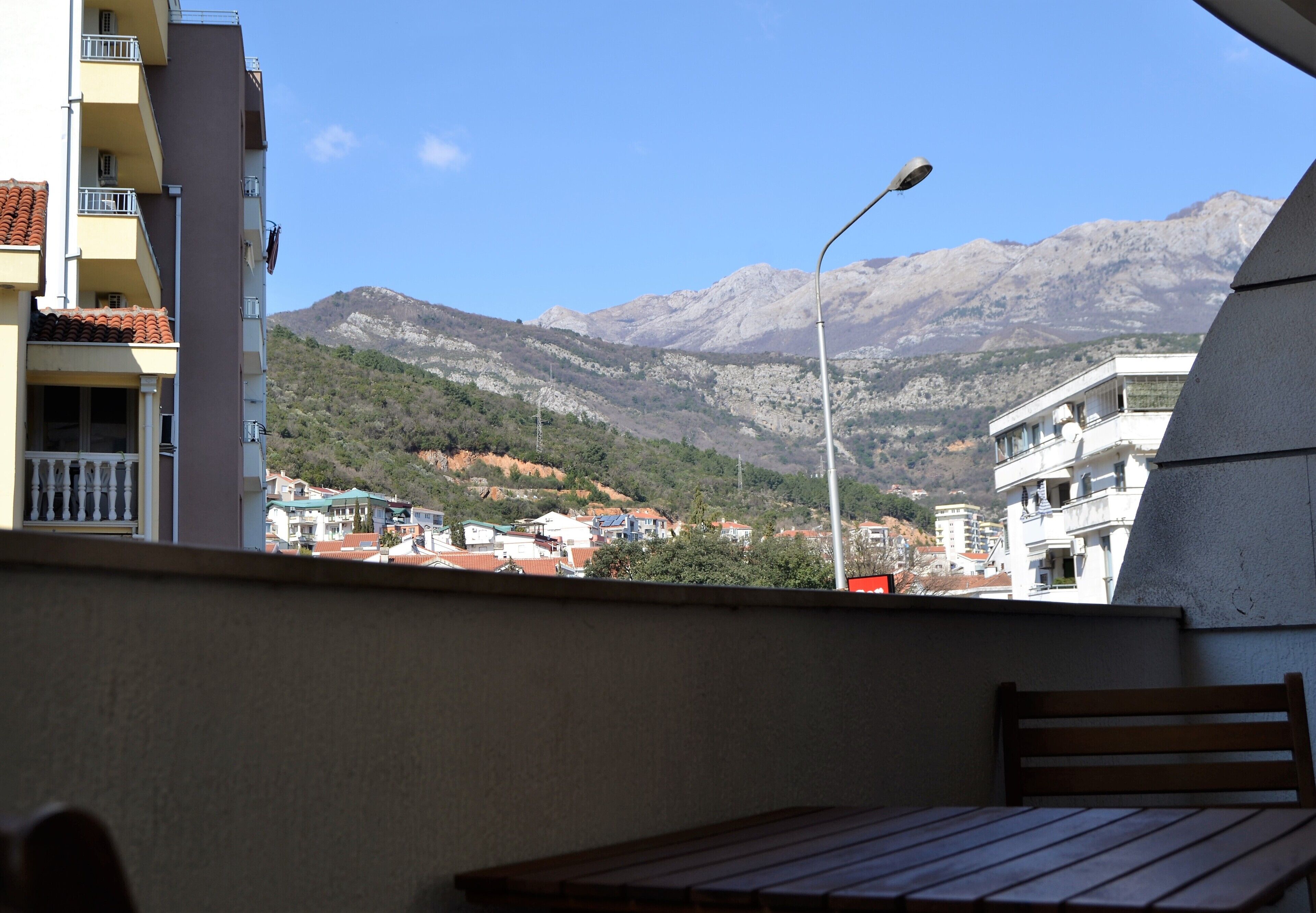 A balcony with a view of a mountain range, a street lamp, and buildings in the background.