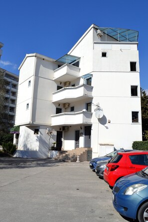 Un immeuble à plusieurs étages, doté de balcons et d’un espace de stationnement où sont garées des voitures.