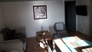 Een woonkamer met een bank, een salontafel, een aan de muur bevestigde televisie en een ingelijste foto.