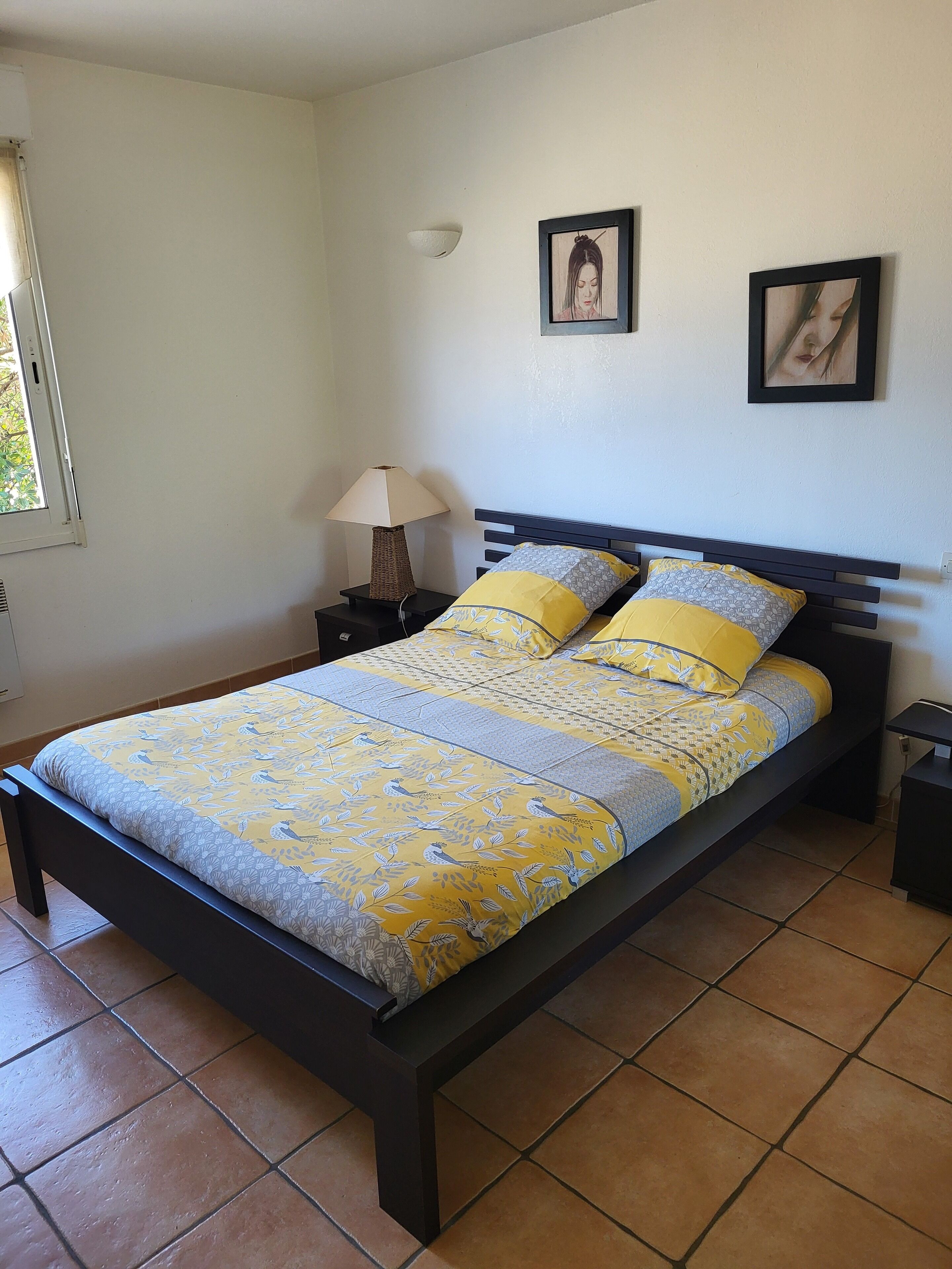 Un lit avec une couvre-lit à motifs, deux oreillers, une lampe de chevet et deux tableaux encadrés accrochés au mur.