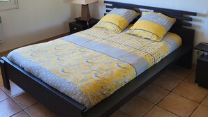 Een bed met een gebedruid laken, twee kussens, een bedlampje en twee ingelijste foto's aan de muur.