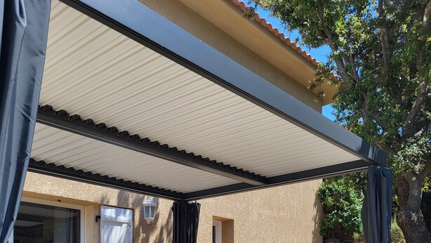 Een terras buiten met rieten meubilair, een overdekte zithoek en uitzicht op het huis.