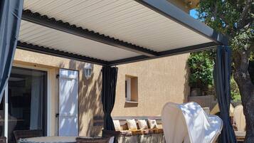 Une terrasse extérieure avec des meubles en osier, un espace salon abrité et une vue sur la maison.