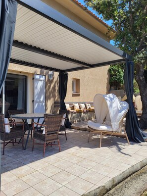 Un pati exterior amb mobiliari de vimet, una zona de seients coberta i vista a la casa.
