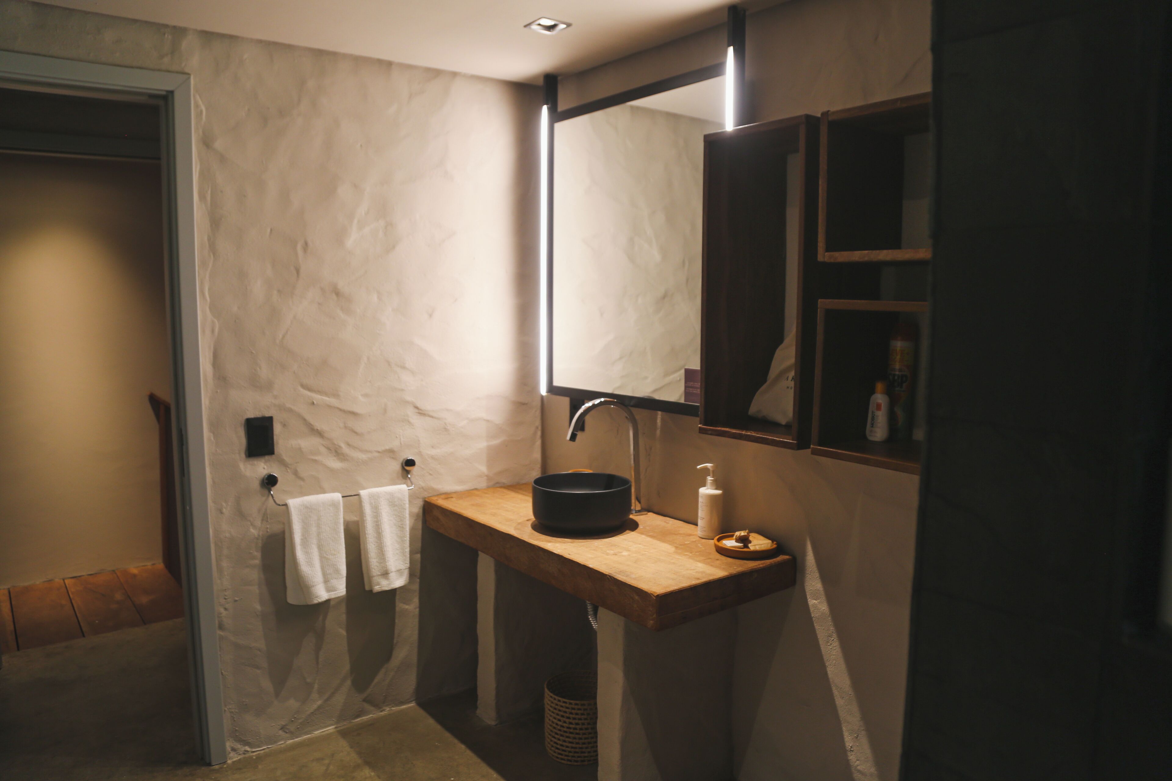 A bathroom with a wooden vanity, a black basin, a mirror, and a towel rack.