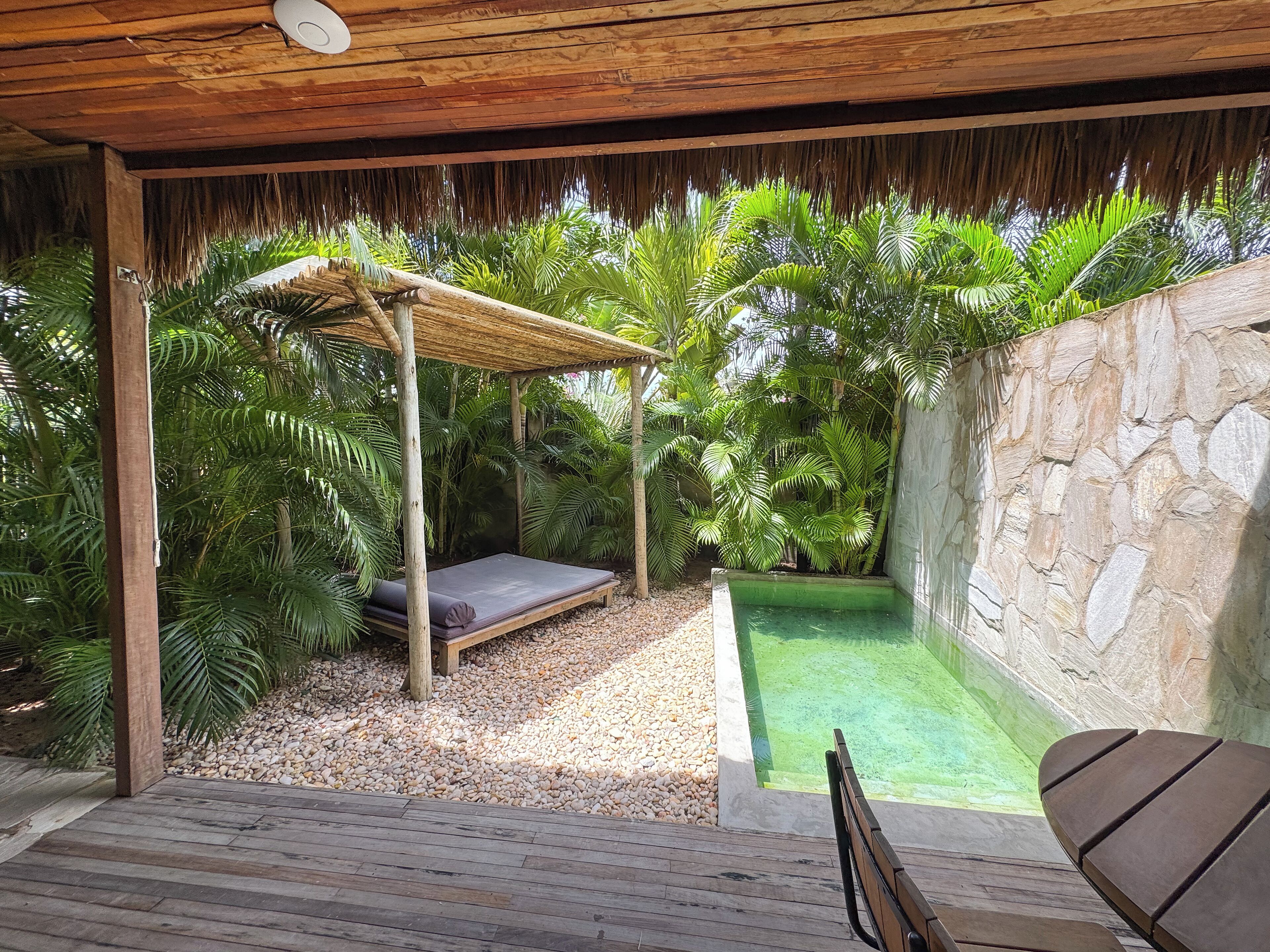 A wooden deck with a thatched roof, a small pool, and lush greenery.