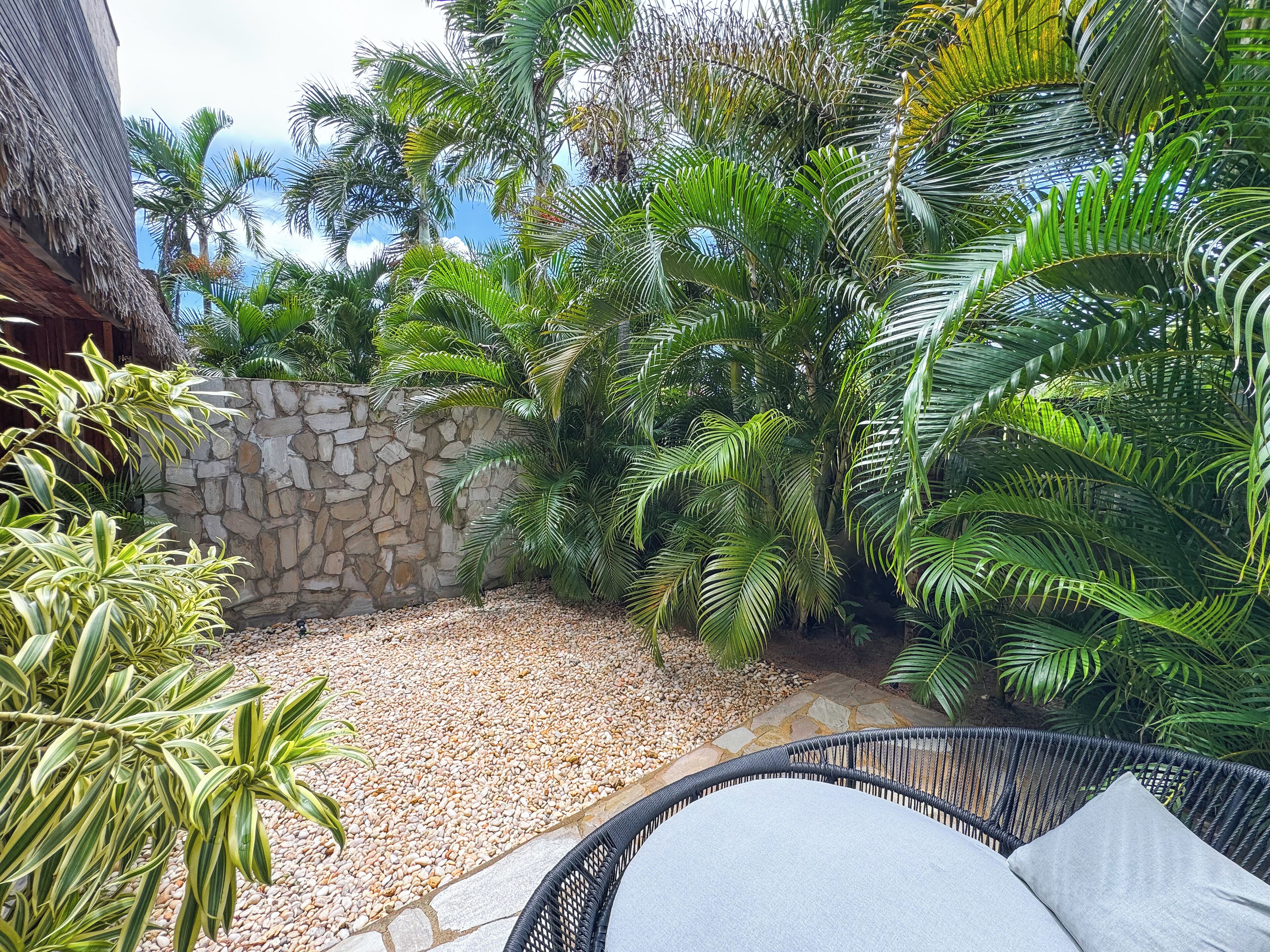 A patio area with a stone wall, tropical plants, and a wicker chair.