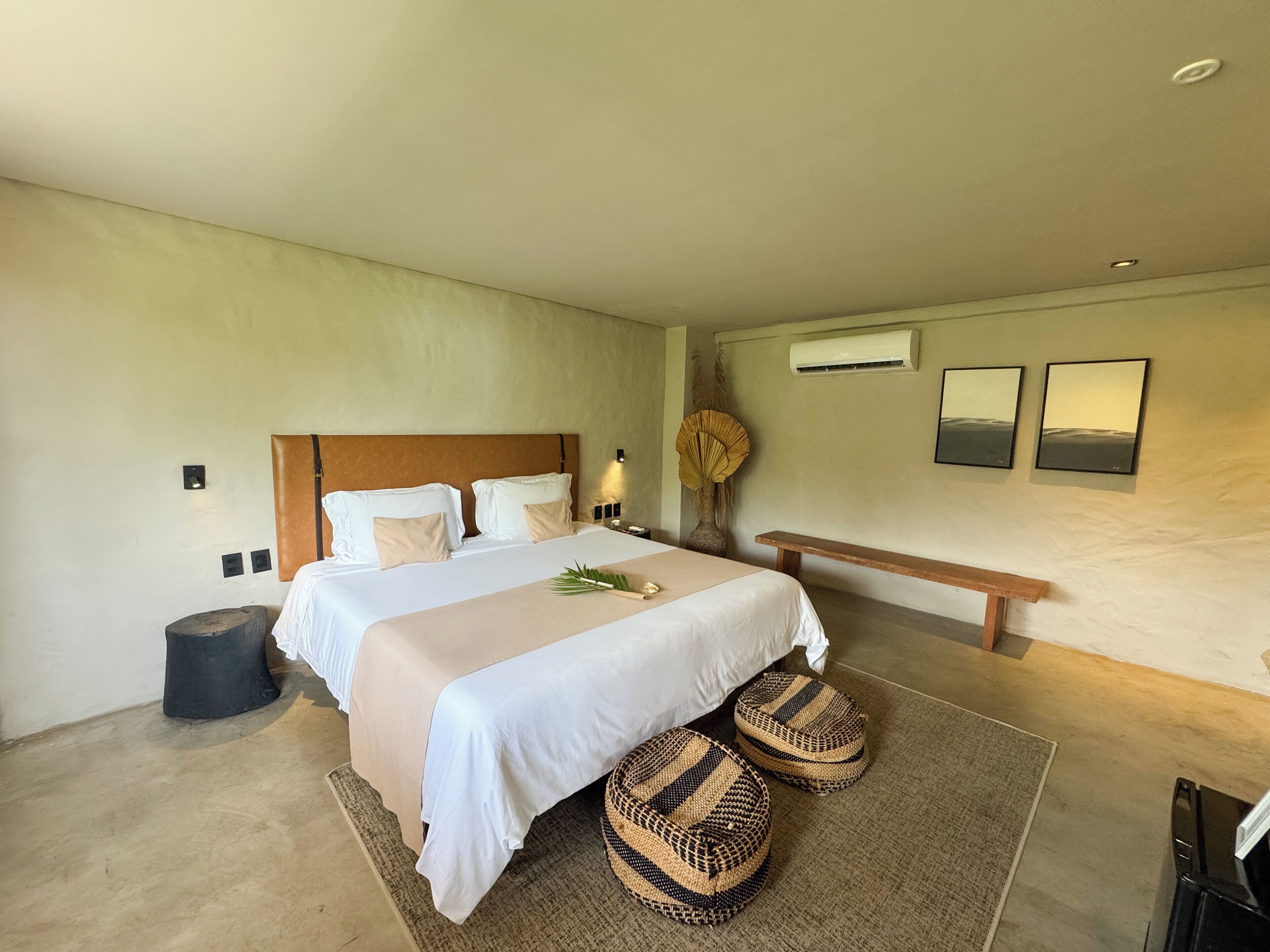 Une chambre moderne avec un grand lit, des tables de chevet, un appareil de climatisation et deux tableaux encadrés accrochés au mur.