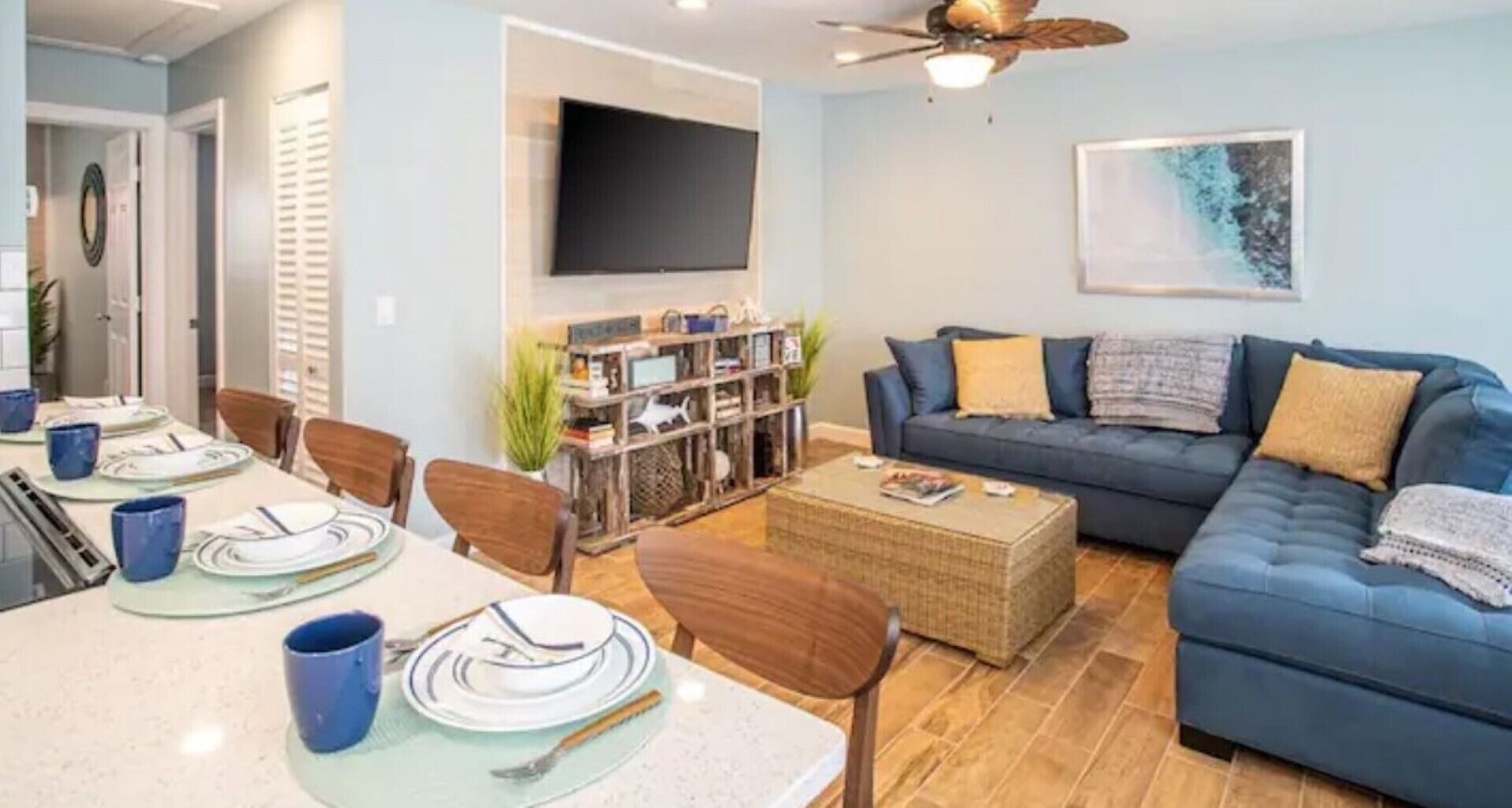 A living room with a blue sofa, a coffee table, and a TV mounted on the wall.