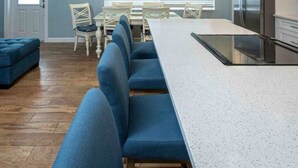 Eine moderne Küche mit einer langen Arbeitsplatte, einem Kühlschrank und einem Essbereich mit blau gepolsterten Stühlen und einem weißen Tisch.
