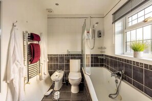 A bathroom with a bathtub, toilet, and shower. There is a window with a plant on the windowsill.