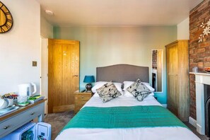 A bedroom with a bed, a nightstand, a dresser, a clock, and a brick wall.
