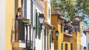 A narrow cobblestone street lined with colorful buildings, balconies with flower pots, and a clear blue sky. - In the Funchal Old Town, near beach - Casa Caetano (Funchal)