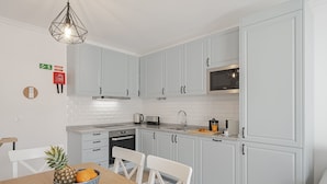 A modern kitchen with white cabinets, a microwave, and a granite countertop. There is a bowl with a pineapple and an orange on the table. - In the Funchal Old Town, near beach - Casa Caetano (Funchal)