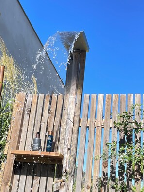 A wooden fence with a water spout and two water containers on a shelf.