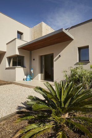 Une maison moderne avec un toit plat, un auvent en lattes de bois au-dessus de l’entrée et une petite fenêtre sur le côté.