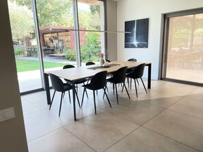 A modern dining area with a large table and chairs, a view of the outdoors, and a painting on the wall.
