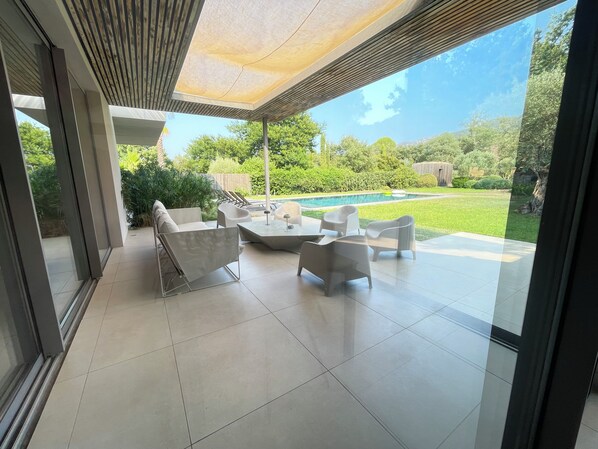 A modern outdoor patio area with a pool, surrounded by greenery and a clear sky.