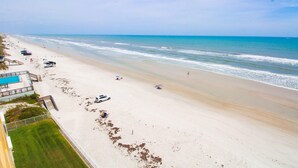 Une plage avec un espace piscine, quelques voitures garées et une vue dégagée sur l’océan.