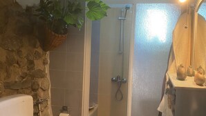 Et badeværelse med toilet, håndvask, brusebad og en hængende plante.