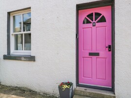 A white building with a pink door and a window with a 'Please do not park' sign.