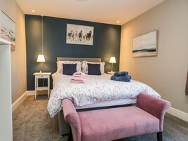 A bedroom with a bed, two bedside lamps, a nightstand, a pink chair, and artwork on the walls.