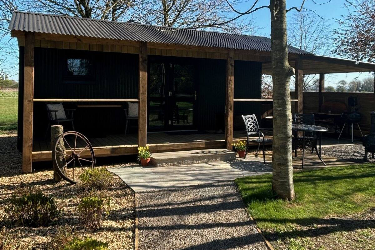 A rustic cabin with a covered porch, outdoor seating, and a stone pathway leading to the entrance.