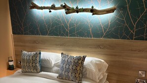 A neatly made bed with patterned pillows, a wooden headboard, and a branch decoration. - Heywood Glamping (Ormskirk)