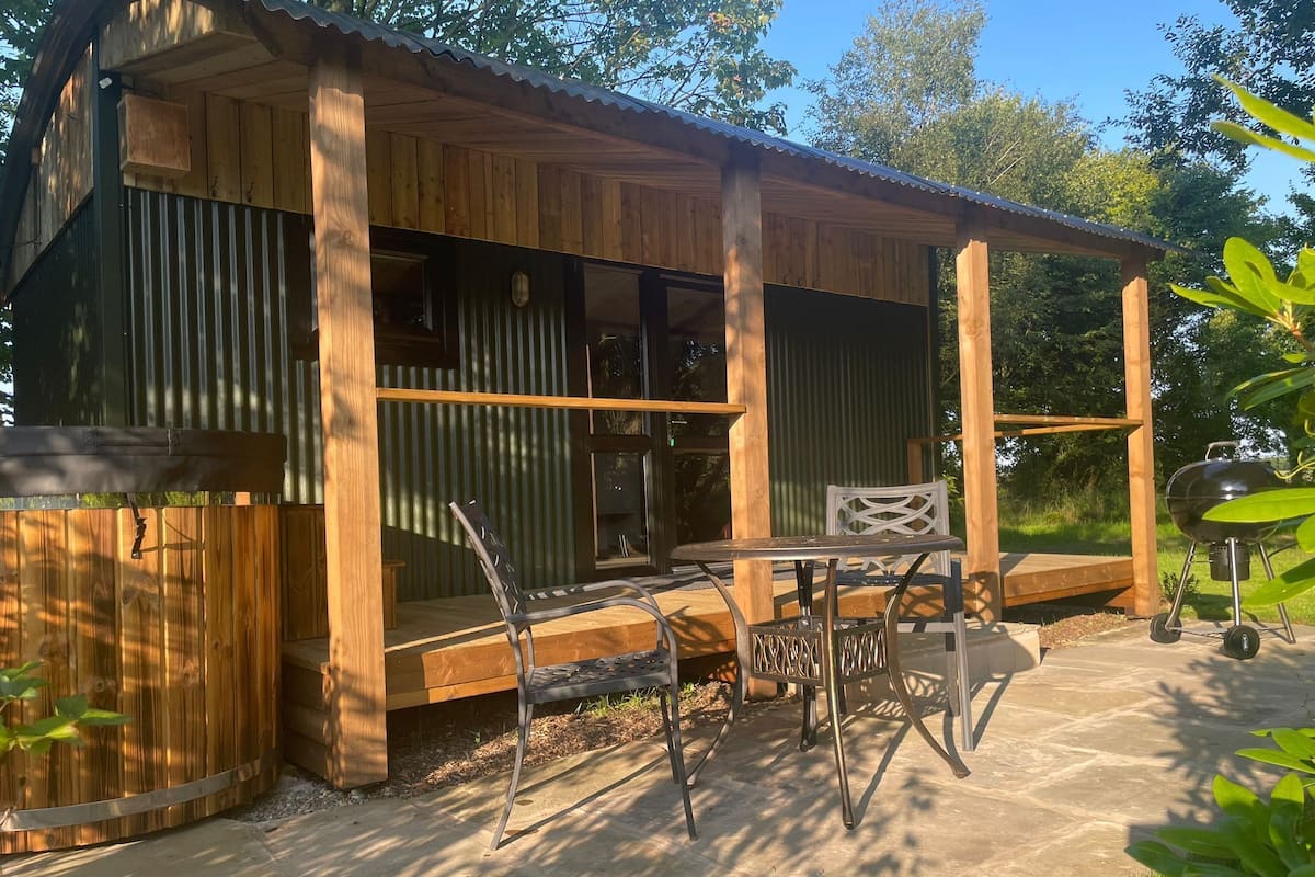 A wooden cabin with a covered patio, a table, and chairs.