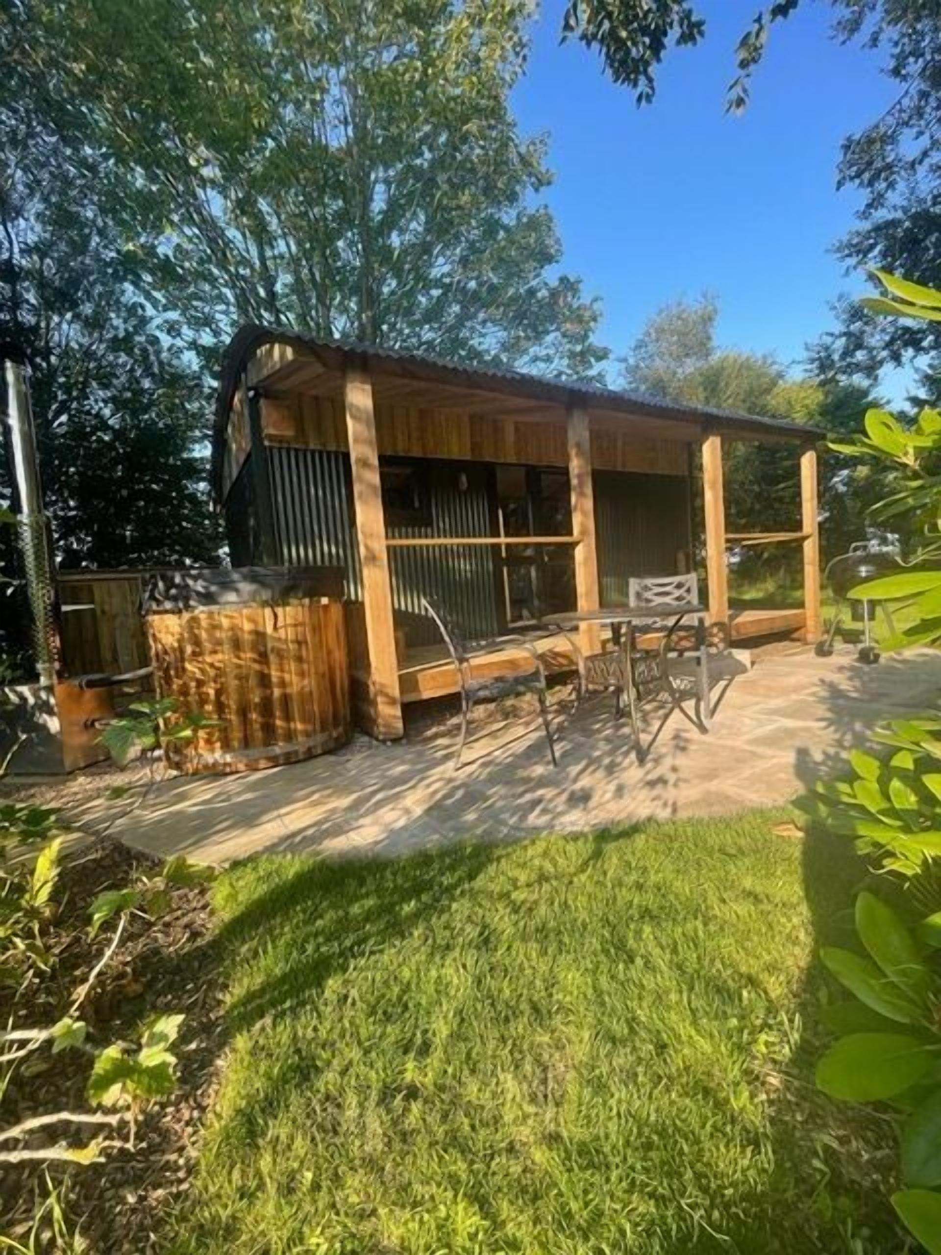 A wooden outdoor structure with a covered patio area, a grill, and a seating arrangement.