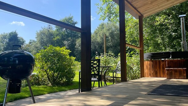 An outdoor patio with a wooden deck, a grill, and a covered seating area. - Heywood Glamping (Ormskirk)