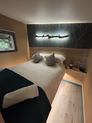 Ein Schlafzimmer mit Bett, Kissen, Nachttisch, Wandleuchte und Fenster.