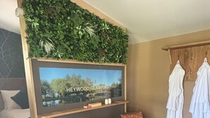 A modern room with a bed, a TV mounted on a wooden wall, a small wooden table with two chairs, and a blue rug on the floor. - Heywood Glamping (Ormskirk)
