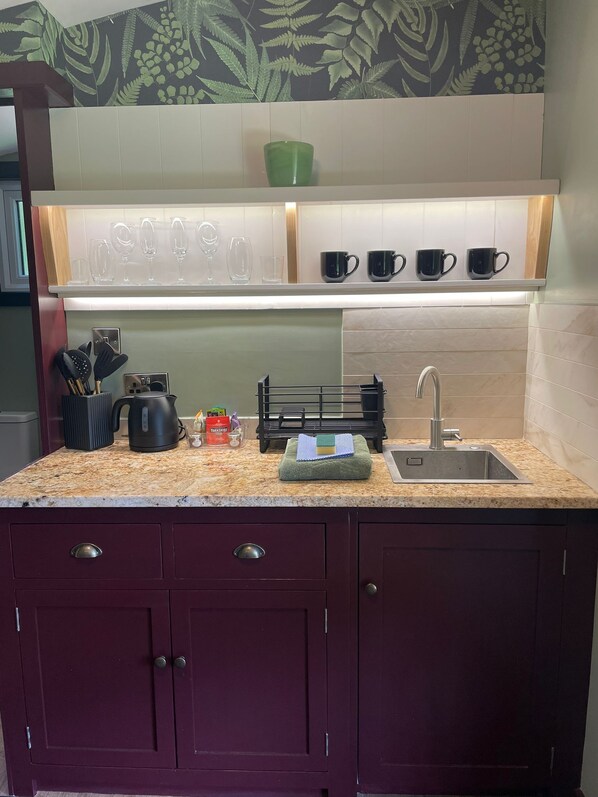 Una cocina con encimera de granito, un lavamanos y una salpicadura con diseño de hojas. Hay cuatro tazas negras en una estantería sobre la encimera.