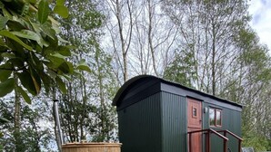 A small wooden cabin with a metal roof, surrounded by a garden with mulch and small plants. - Heywood Glamping (Ormskirk)