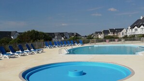 Una piscina con sillas reclinables azules y un muelle de madera.