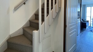 Una escalera con barandales y pasamanos blancos, que conduce a una habitación con piso de madera oscura y un ventanal grande.