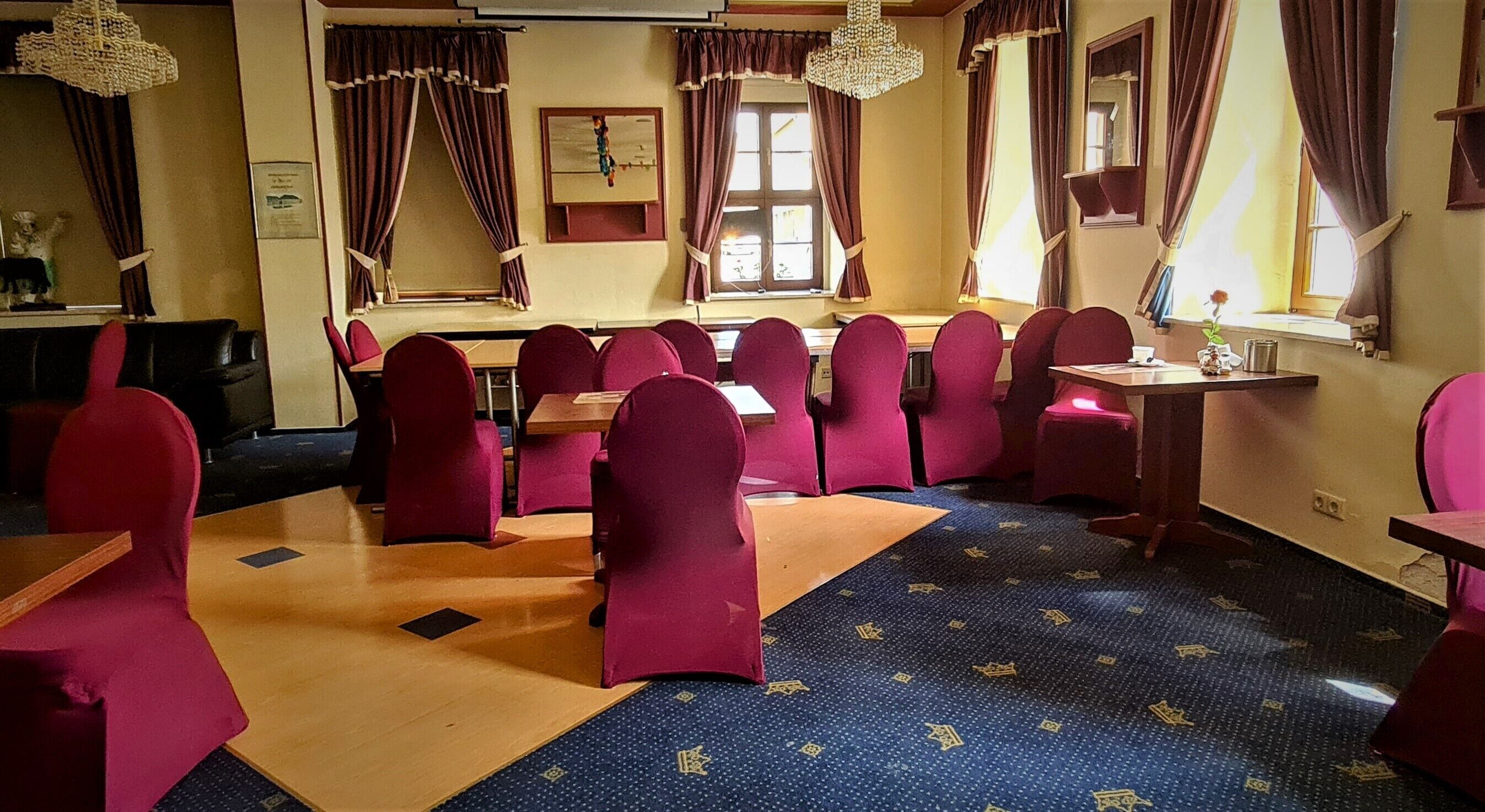 A dining area with red chairs and tables, a patterned carpet, and a window with curtains.