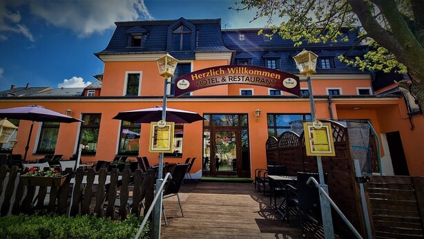 Ein Hotel Eingang mit Außenbereich und einer Schilder mit der Aufschrift 'Herzlich Willkommen Hotel & Restaurant'.