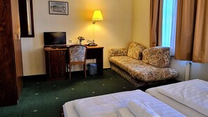 Ein Hotelzimmer mit Bett, Sofa, Schreibtisch mit Lampe, Fernseher und einem Bild an der Wand.