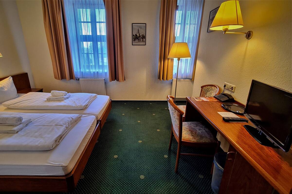 Une chambre d’hôtel avec deux lits, un bureau avec un ordinateur et deux lampes.