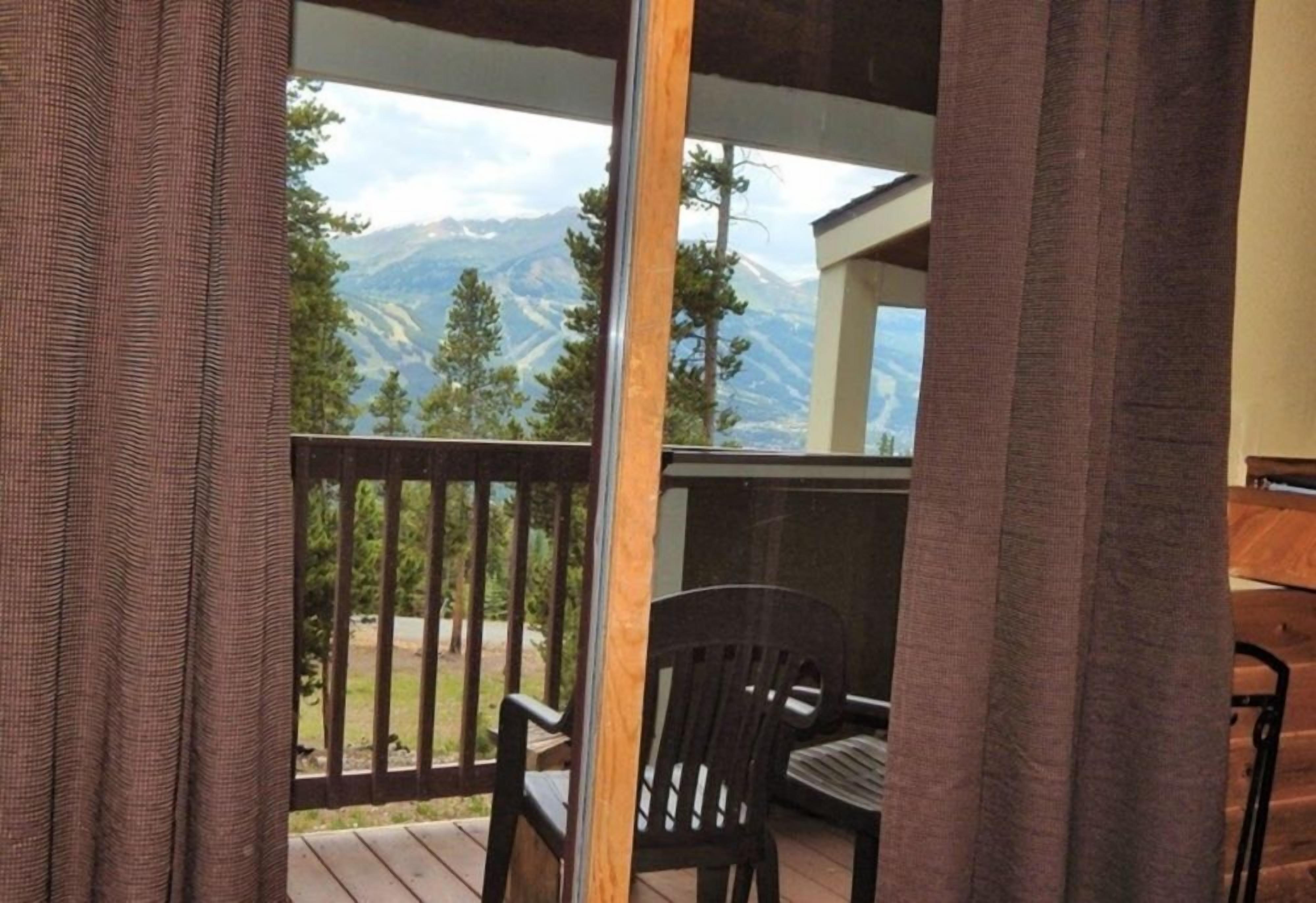Un balcón con vistas a montañas, una silla y una mesa.